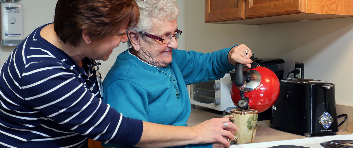 Healthcare worker assiting elderly lasy with poring hot water into her mug