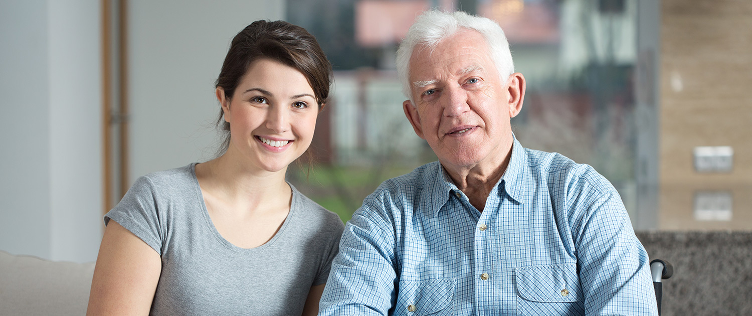 Young pretty female caretaker and elderly man on a wheelchair